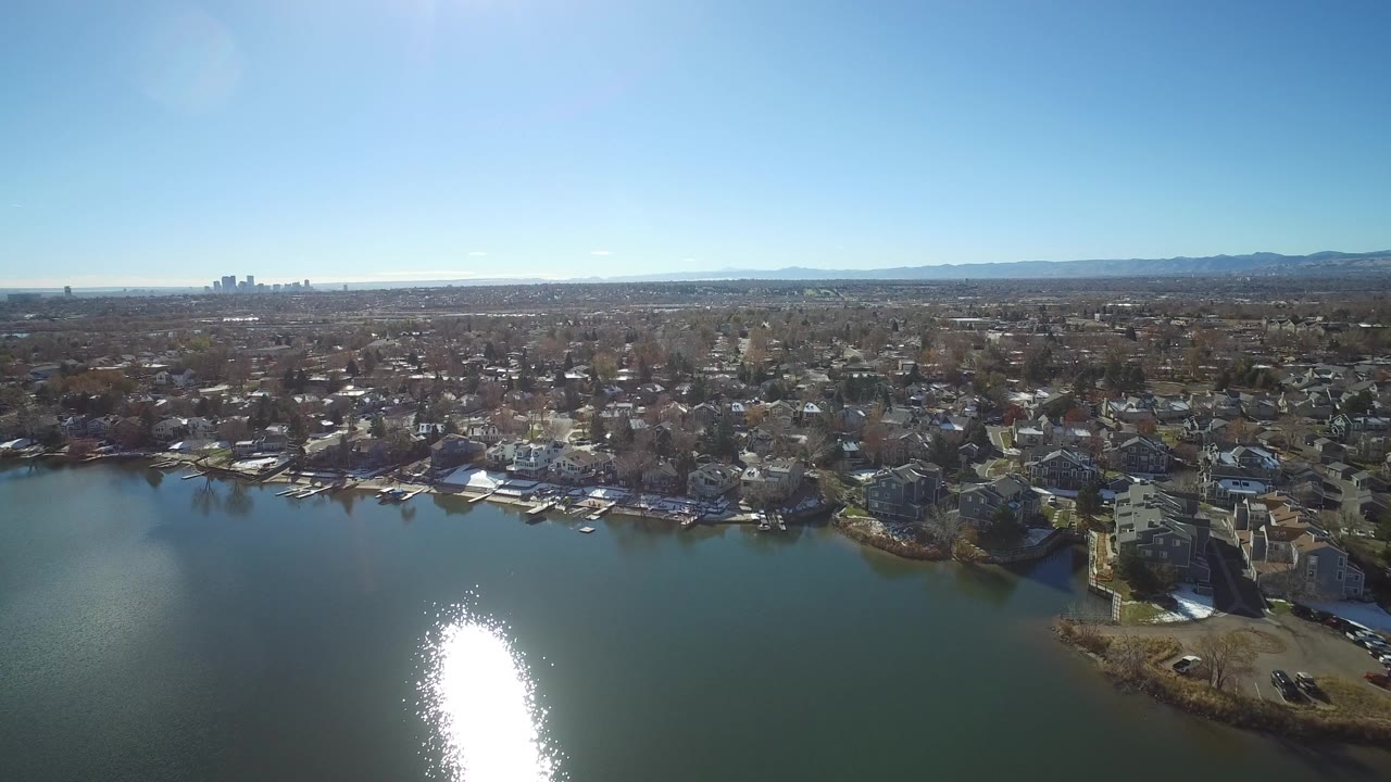 Aerial view of a lake beside suburban homes under a blue sky.