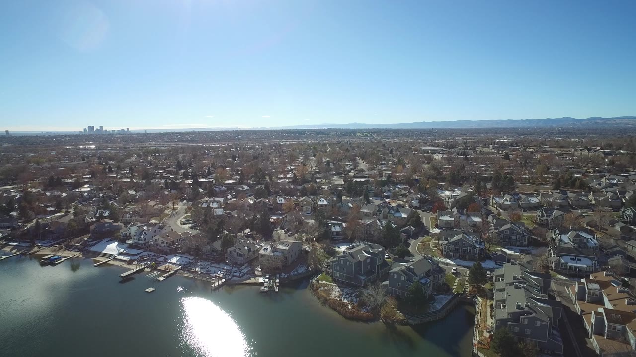 Aerial view of lakefront homes and a wide suburban neighborhood under clear sky.