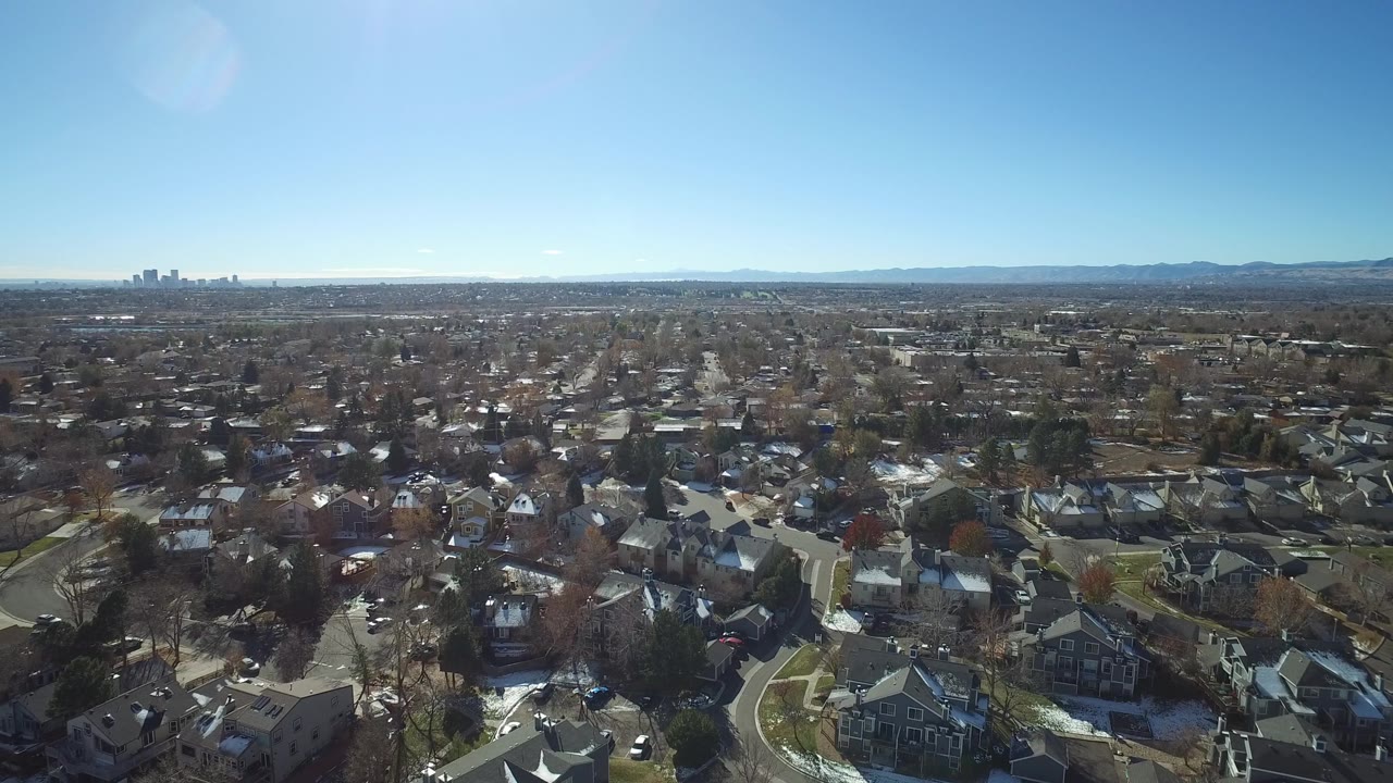 Aerial frame over Westminster, Colorado rooftops and branching roads, with the skyline slightly left of center, the mountain horizon beyond, and no visible people.