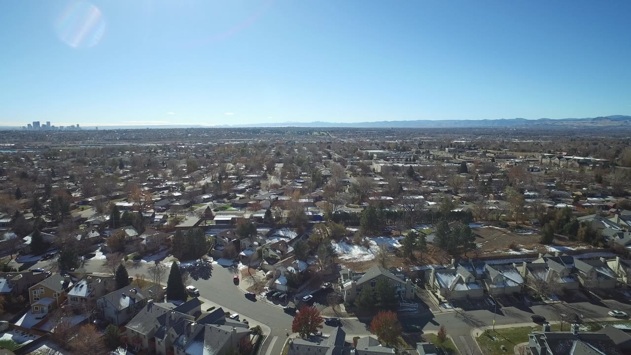 Aerial view over suburban houses toward distant mountains and skyline.