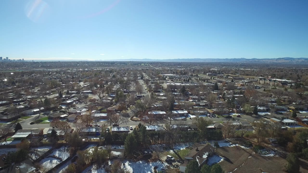 Suburban rooftops and streets seen from above with mountains in the distance.