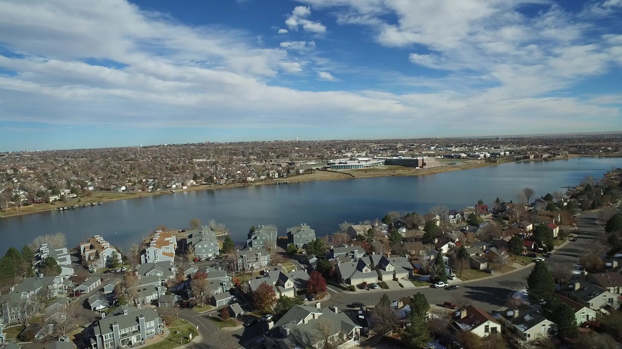Aerial view of suburban houses beside a lake under a partly cloudy sky.