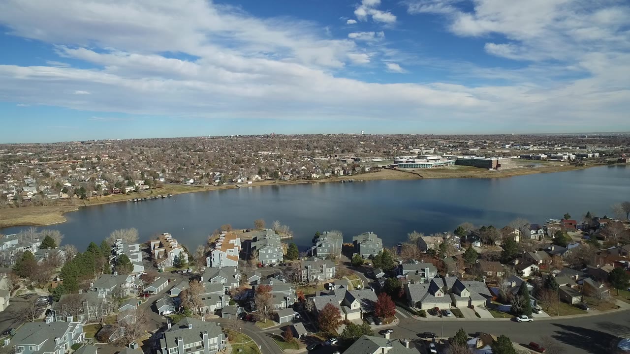 Aerial cityscape with a lake, rooftops, and distant low-rise buildings.