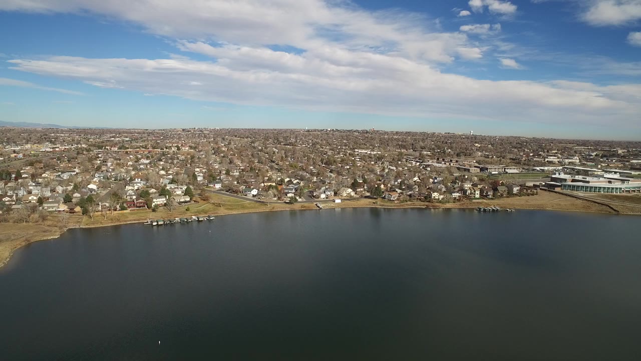 Aerial view over dark water toward suburban homes and a cloudy blue sky.
