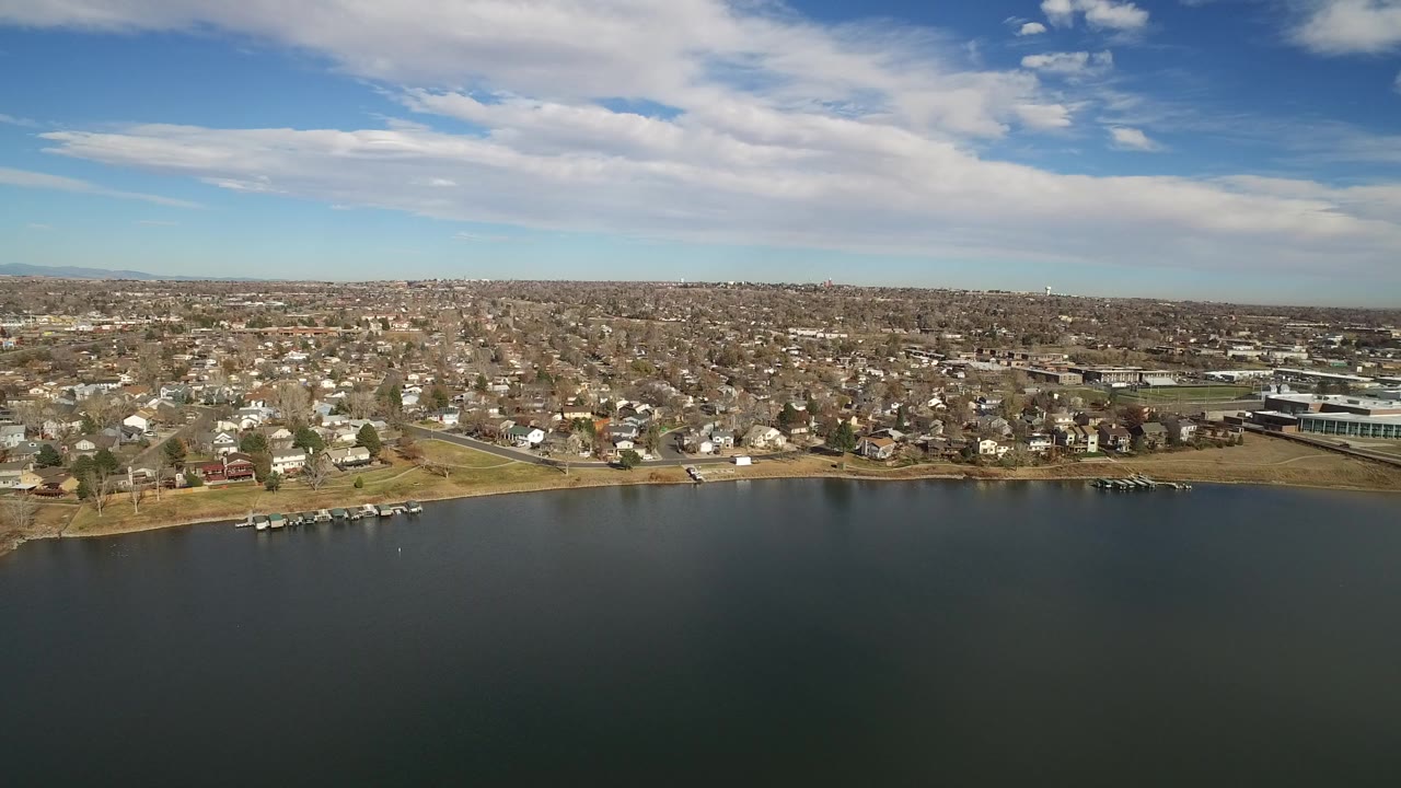Aerial view over dark water toward a suburban shoreline and city grid.