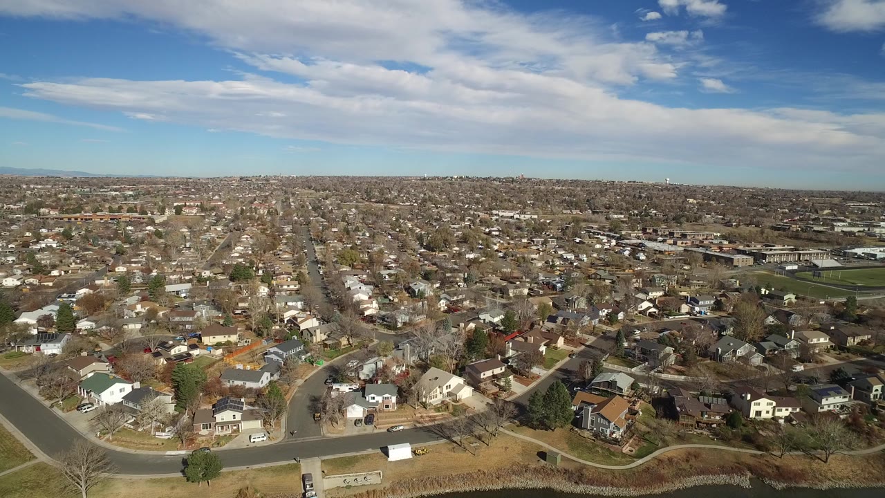 Aerial view over suburban houses and streets under a blue sky.