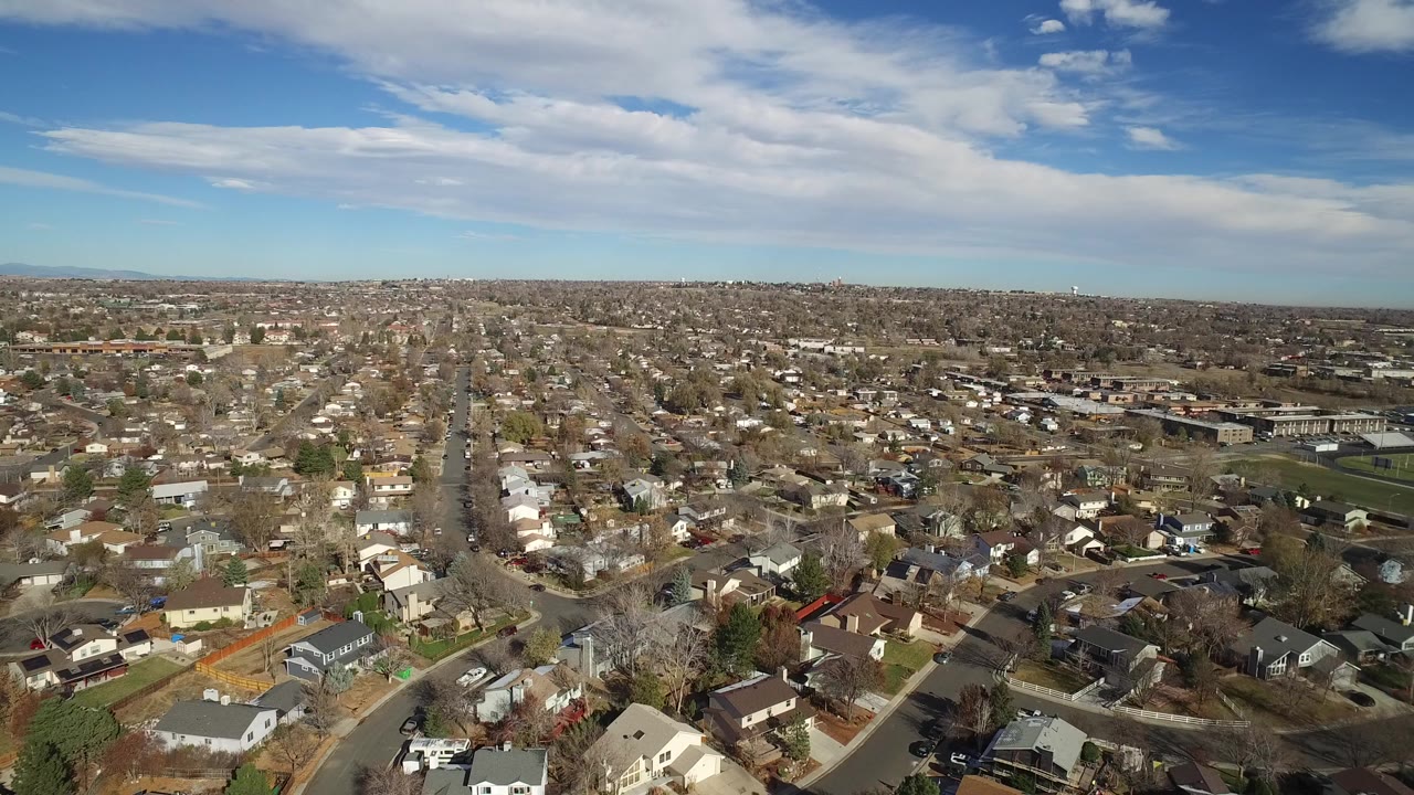 Aerial view over suburban houses and streets beneath a blue sky.