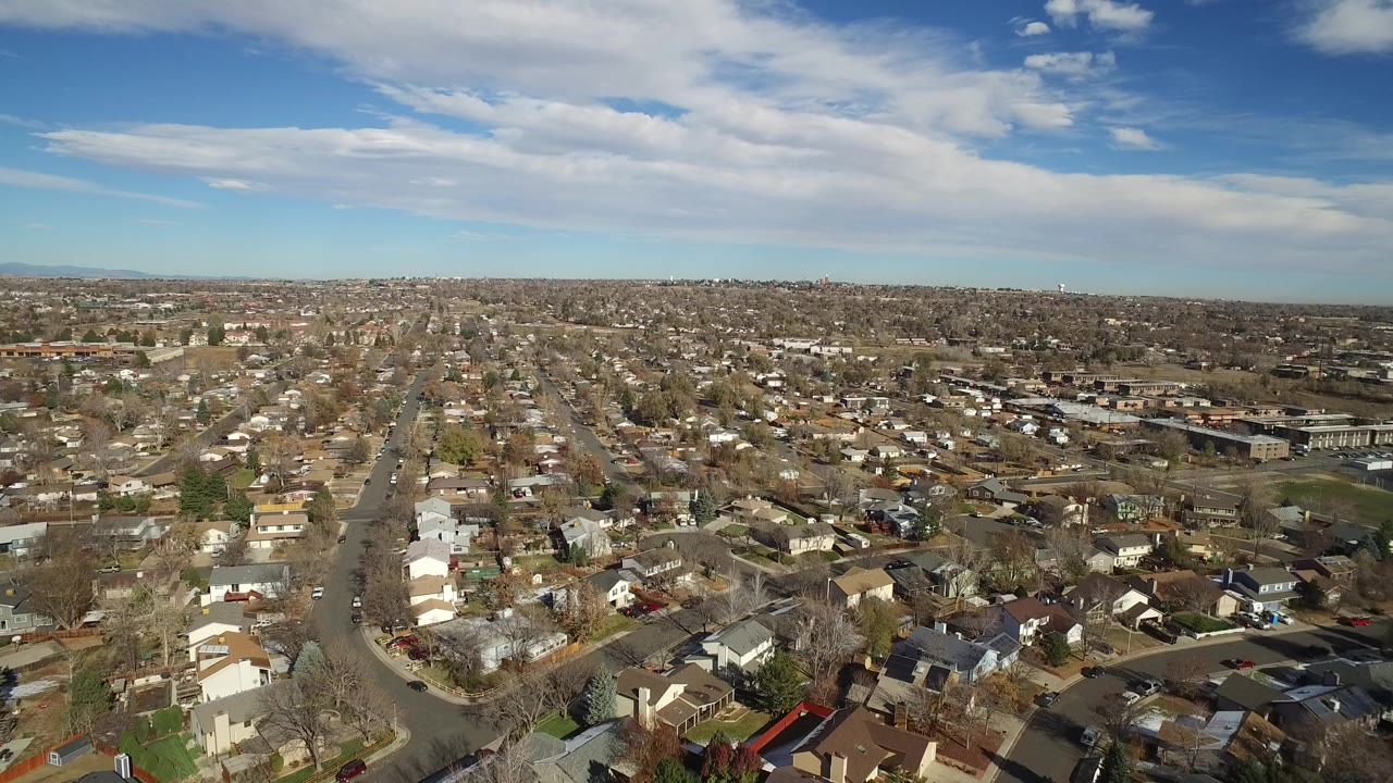 Aerial view over suburban houses and streets under a partly cloudy sky.