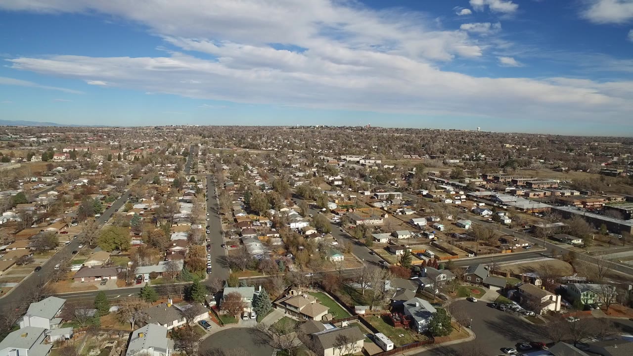 Aerial view over suburban streets and houses under a partly cloudy sky.