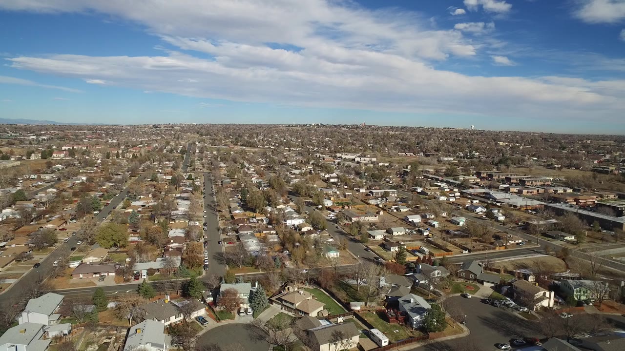 This Westminster, Colorado aerial frame looks across compact residential blocks, brown roofs, scattered trees, and a low horizon, with no visible people.