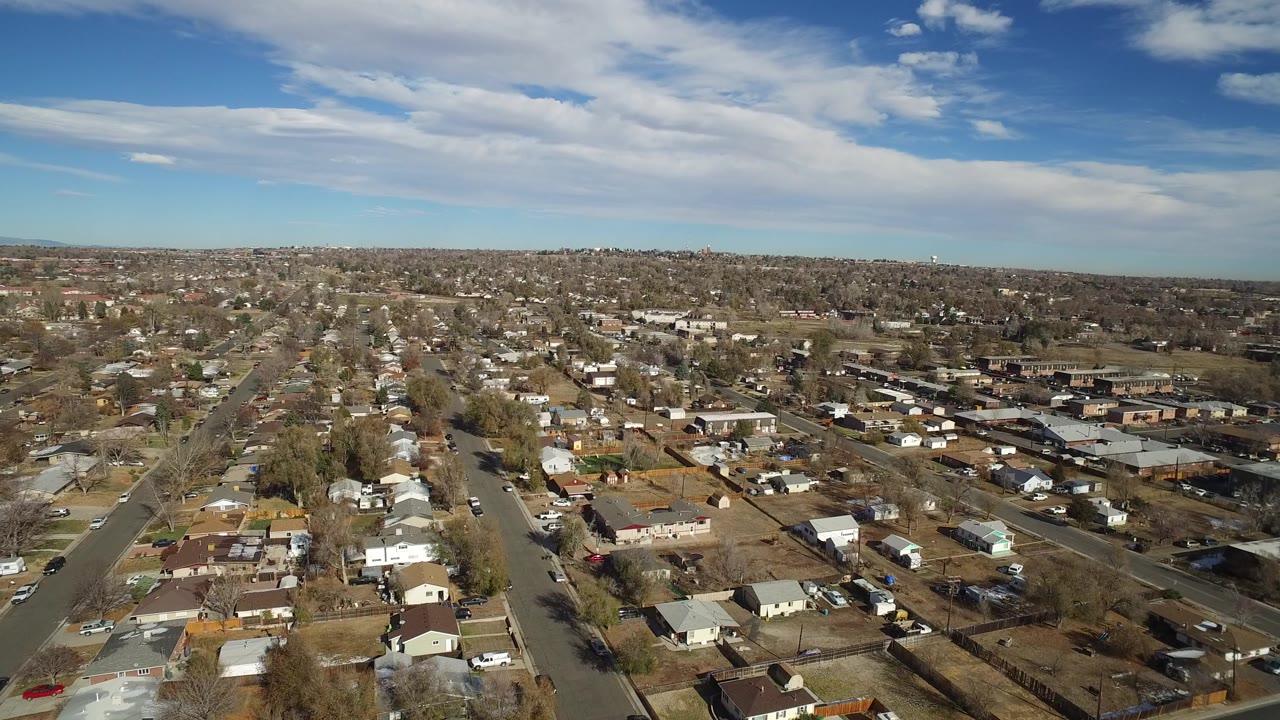 Aerial view over suburban homes and streets under a partly cloudy sky.