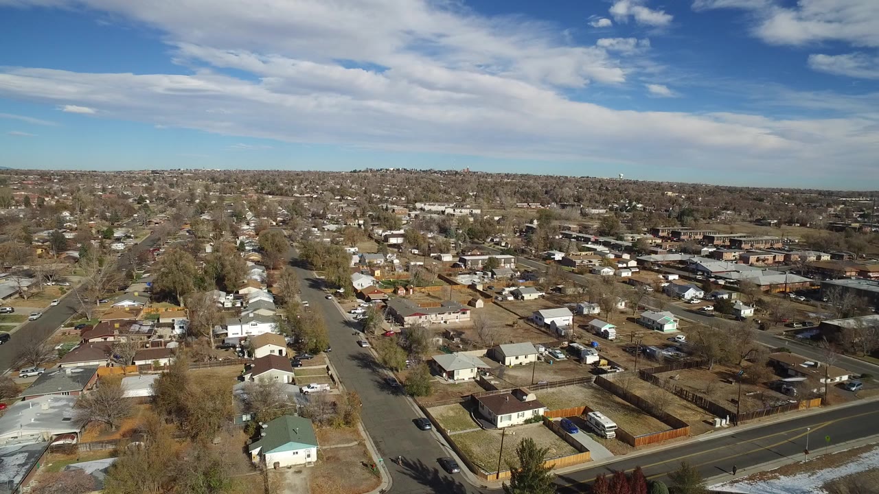 High aerial view over suburban homes and streets under a blue, cloudy sky.
