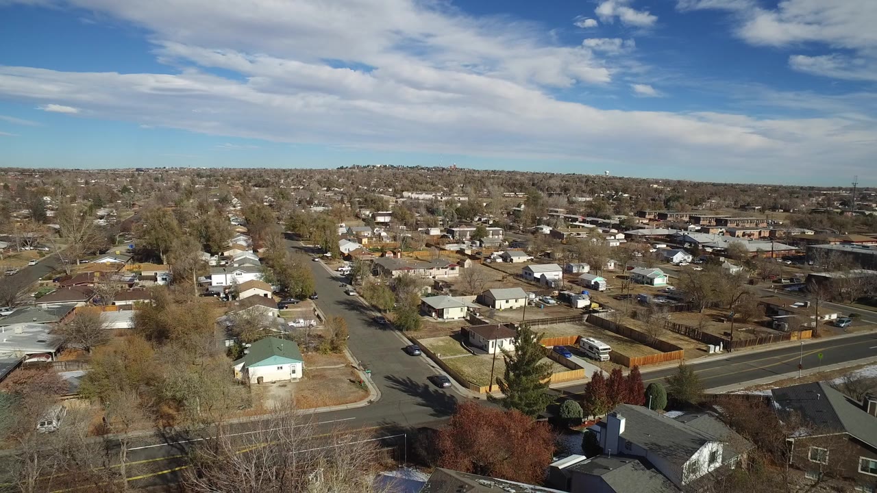 Aerial view across Westminster, Colorado houses and tree-lined streets, with a pale green roof near the lower left and no visible people.