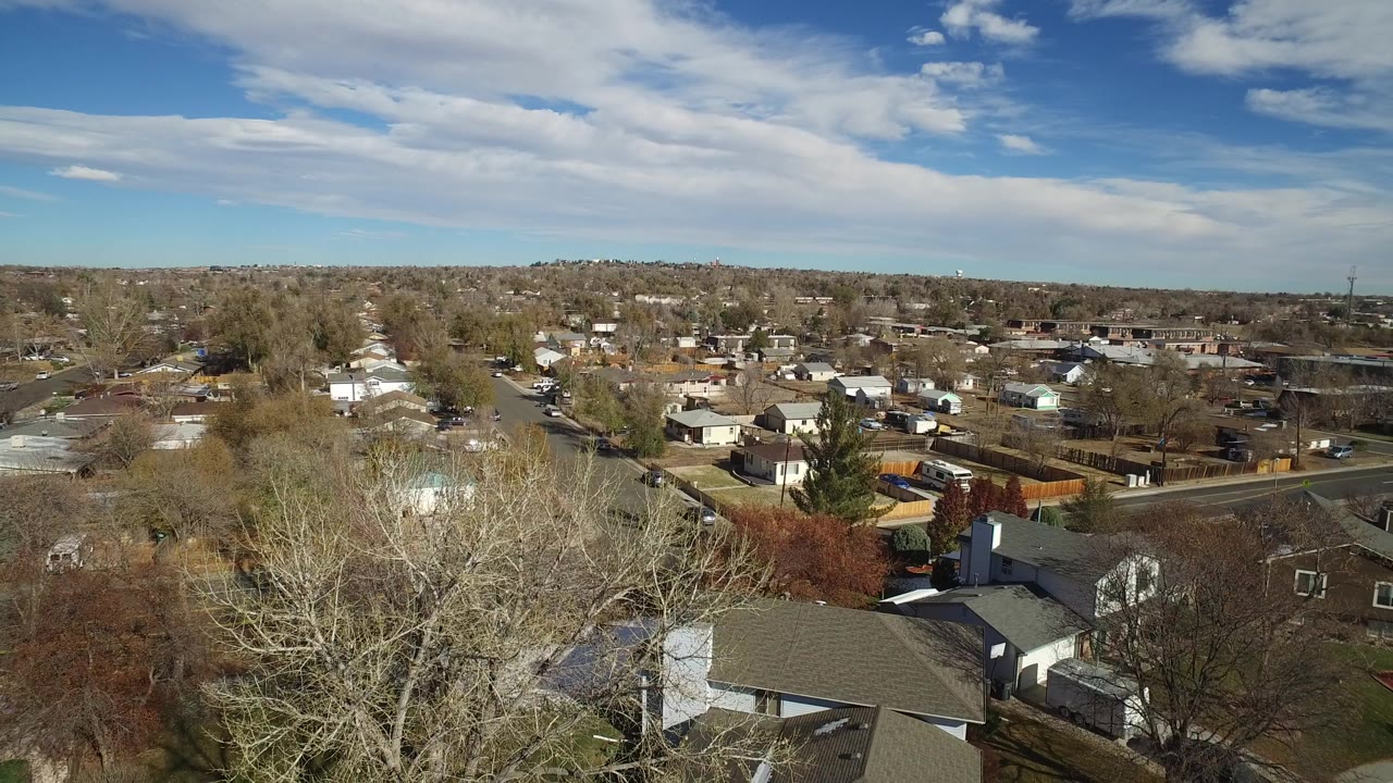Drone-like aerial view of homes and trees across a quiet neighborhood.