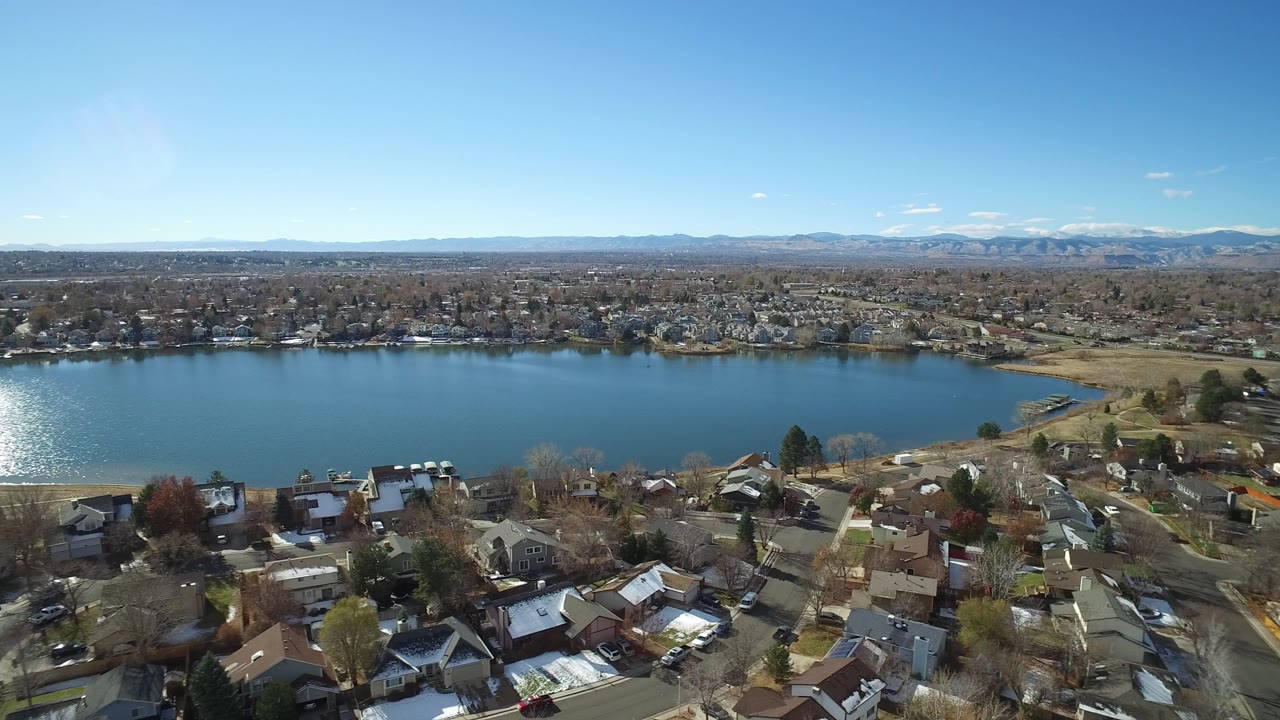 Aerial view over homes toward a blue lake and distant mountains.