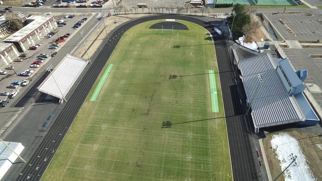 High aerial view of a Westminster, Colorado football field inside a black running track, with bleachers, parking areas, and no visible people.