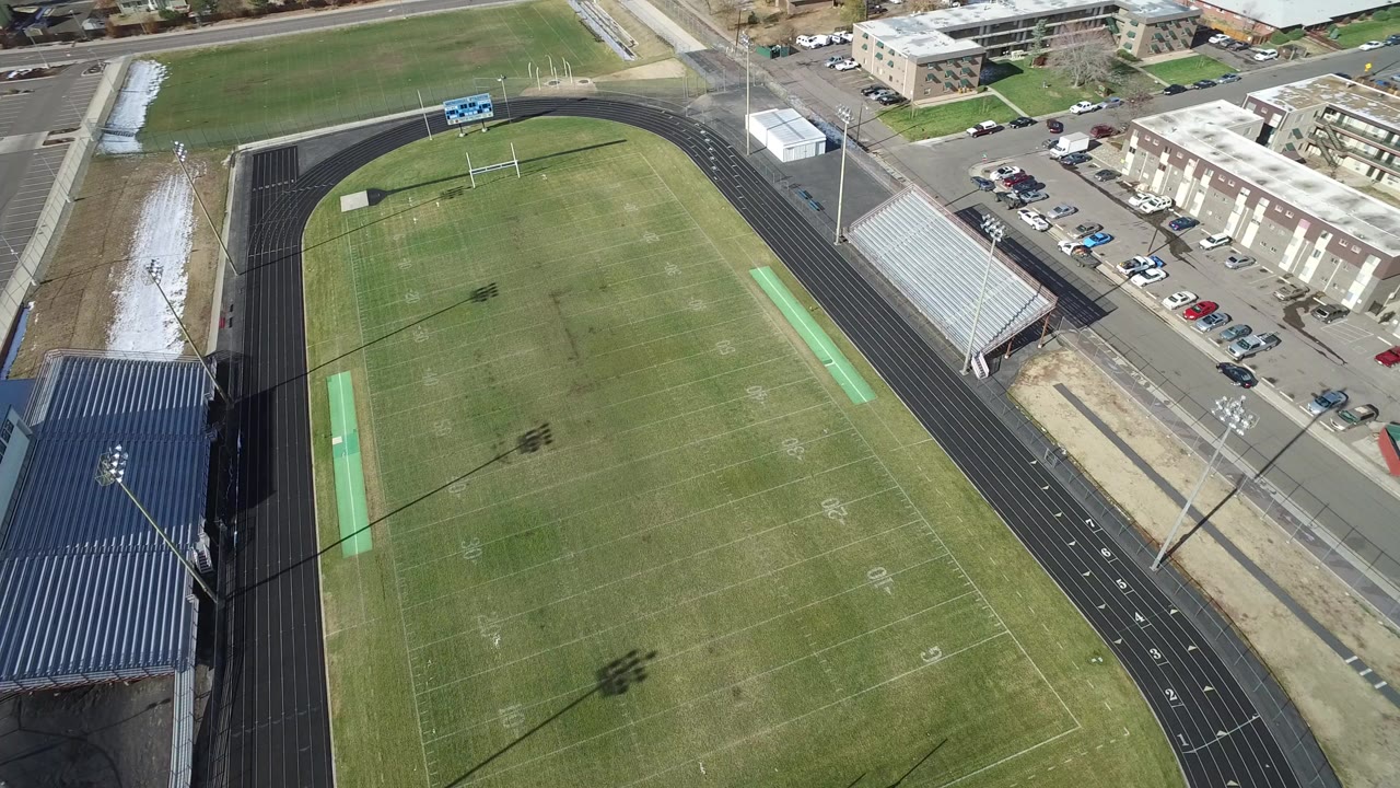 Aerial view of an empty football field and running track beside bleachers.