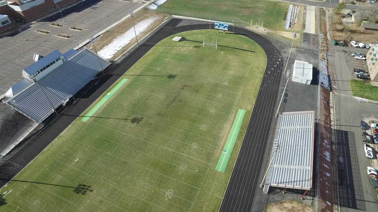 Aerial view of a green athletic field inside a running track with bleachers.