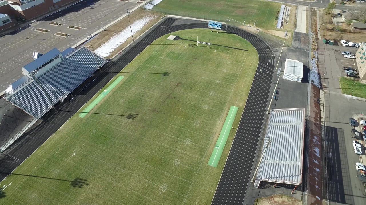 Aerial view of the Westminster, Colorado field from a slightly shifted angle, with the grandstand near the lower left, the oval track curving around the grass, and no visible people.