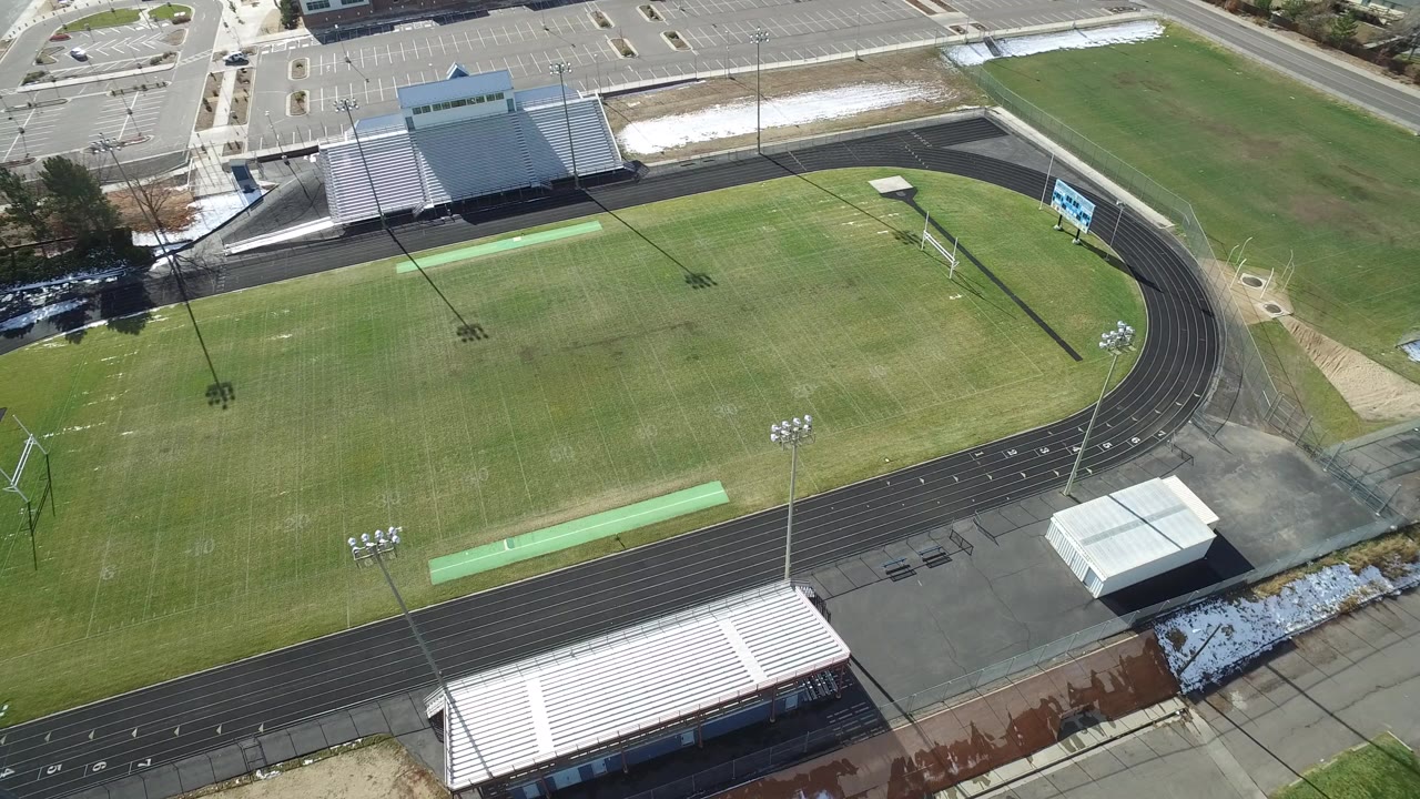 Aerial view of a sports field, running track, bleachers, and parking lot.
