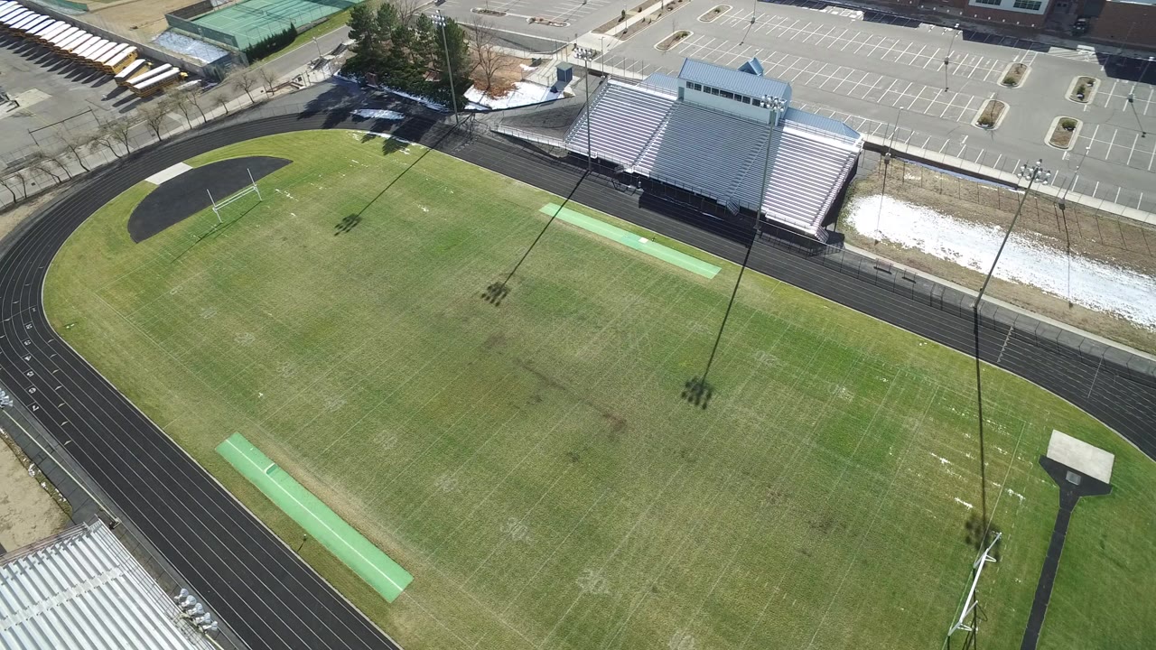 Aerial view of a sports field inside a running track with bleachers and parking nearby.