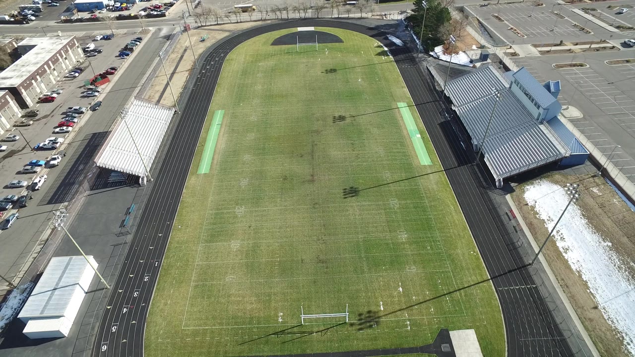 Drone view of an empty football field, track, bleachers, streets, and parked cars.