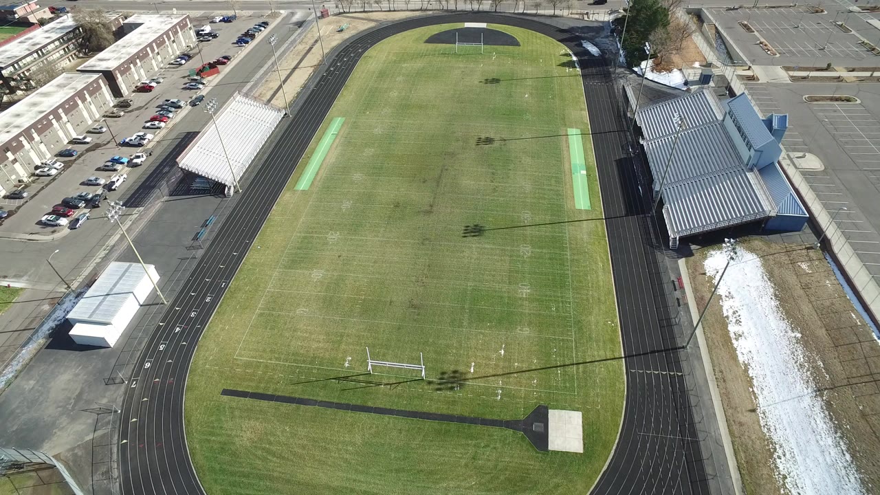 Aerial view of a football field inside a running track with bleachers nearby.