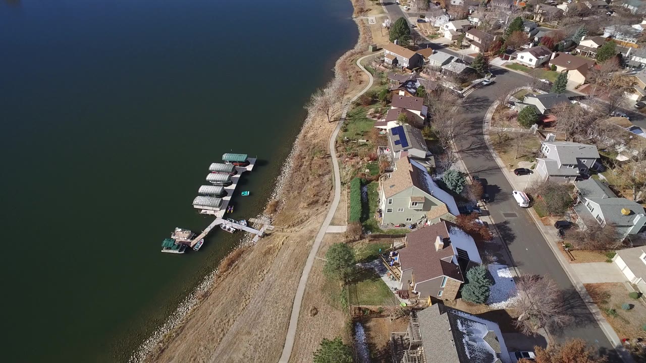 Aerial view of lakeside houses, shoreline path, docks, and dark water.
