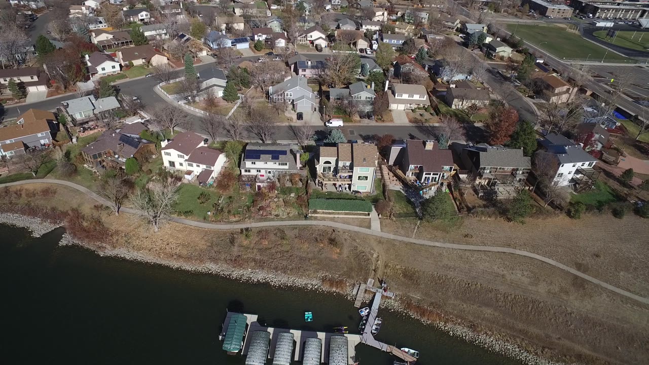 Aerial view of suburban homes by water with docks, boats, roads, and fields.