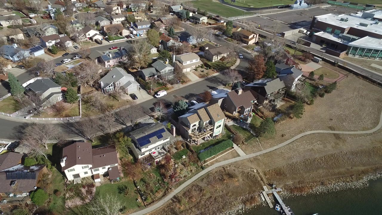 Aerial view of homes, roads, a shoreline path, and lake edge.