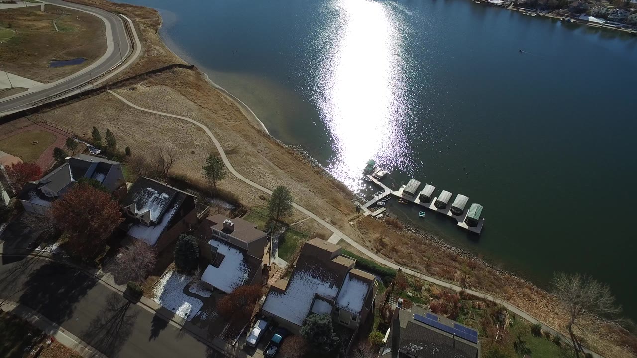 Aerial view of homes beside water with a dock and bright sun reflection.