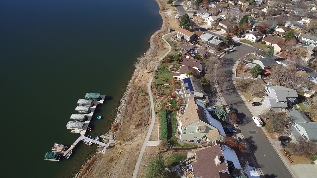 Aerial view of shoreline houses, docks, and dark green water.