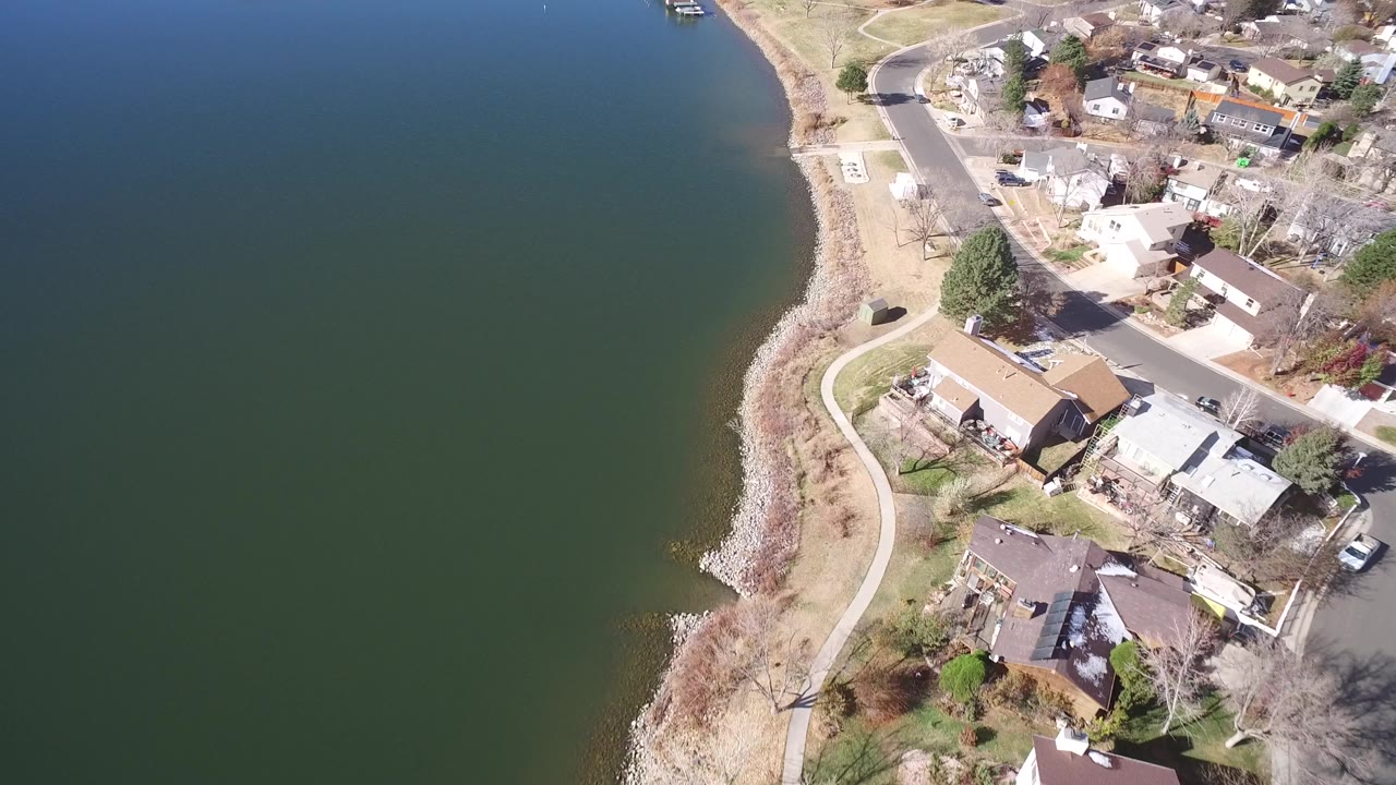 Aerial view of green water, rocky shoreline, path, and nearby homes.