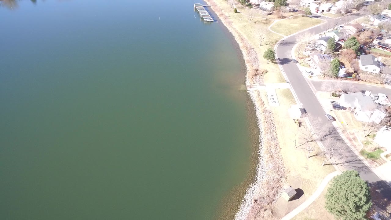 Aerial view of green water beside a rocky residential shoreline.