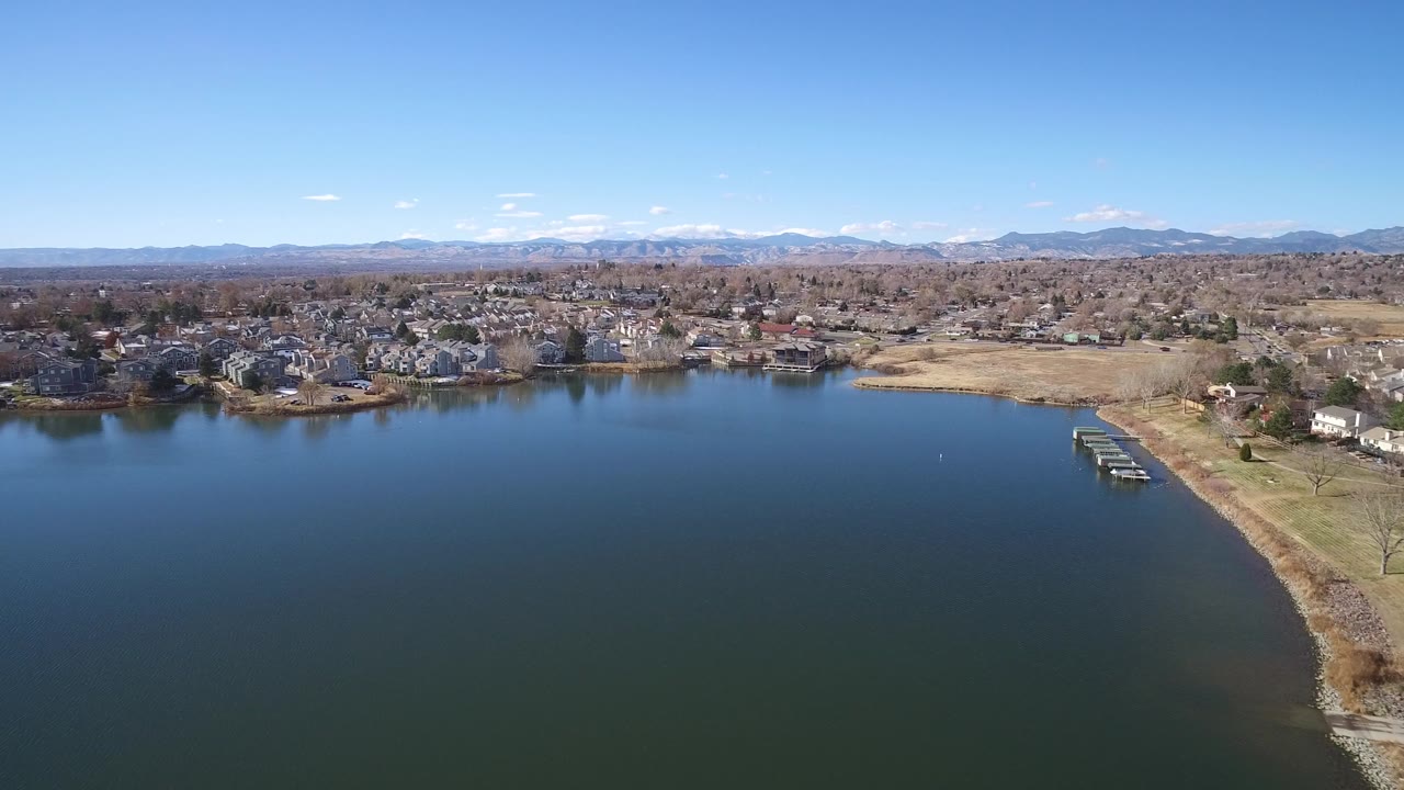 Aerial view of a lake with shoreline homes and distant mountains.
