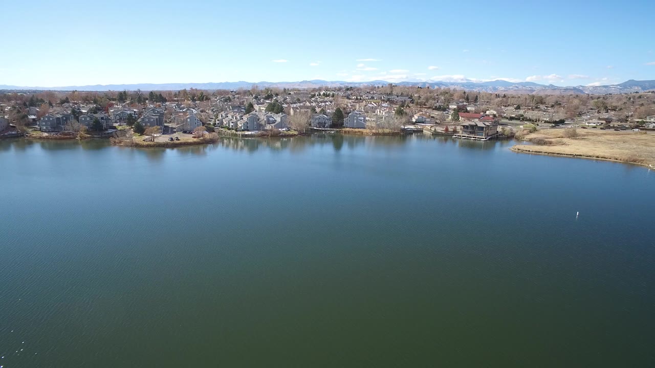 Aerial view over a broad lake with suburban homes and mountains beyond.