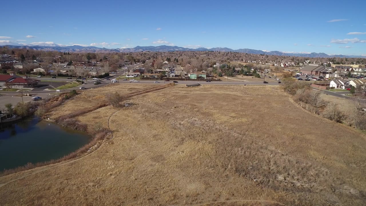 Aerial view of a brown field beside a small lake and highway under a blue sky.