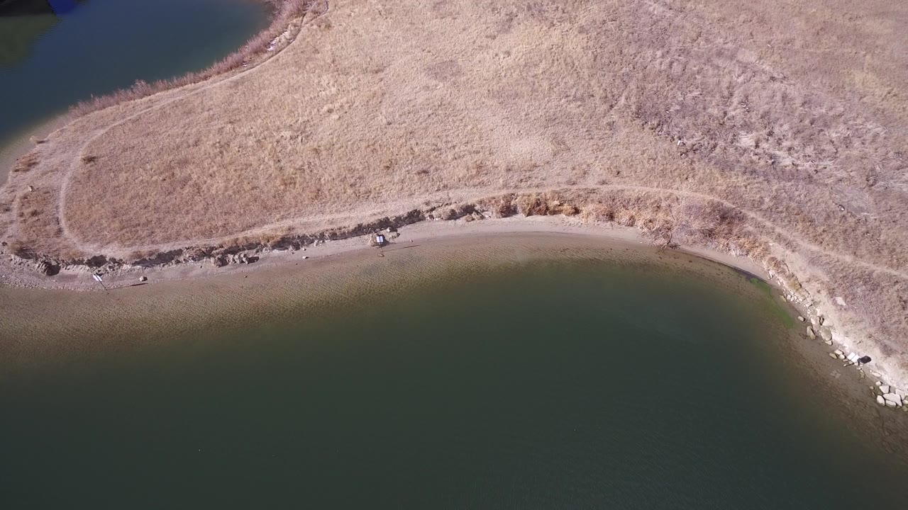 Curved lake edge with rocks, sand, and dry shoreline grass.