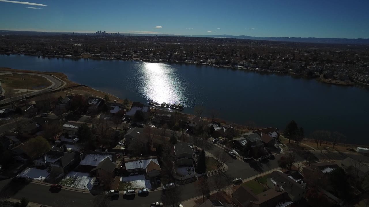 Aerial view over houses beside a wide lake with sun glare on the water.