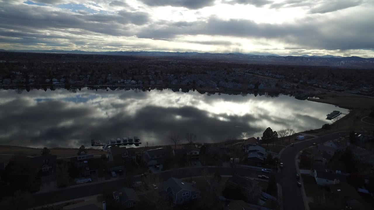 Aerial view of a reflective lake beside houses and roads under cloudy sky.