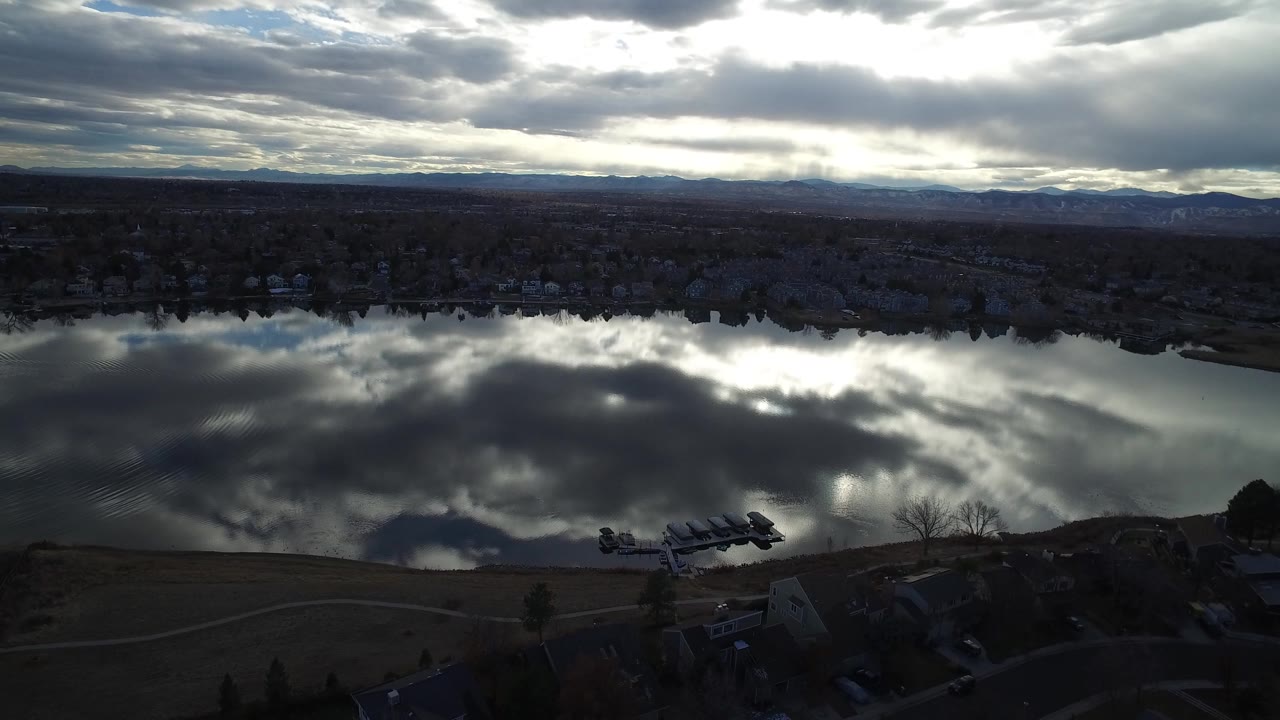 Aerial view of a dark lake reflecting layered clouds beside a residential shoreline.