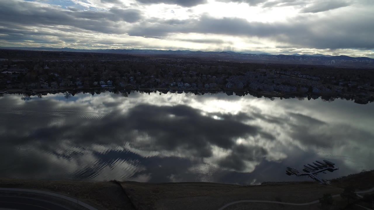 Cloudy sky mirrored in a broad lake with a shoreline and docks near the edge.