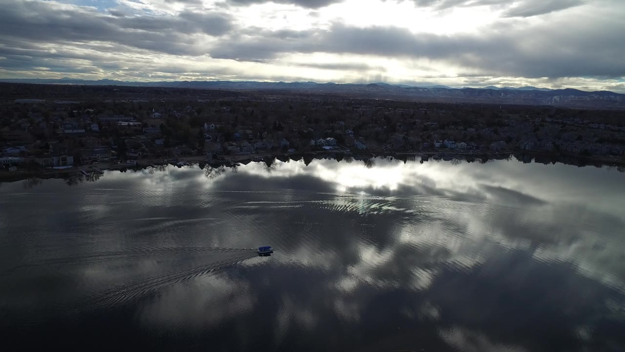 Aerial view in Westminster, Colorado, looking over dark rippling water with bright cloud reflections, a distant shoreline, hills on the horizon, and no visible people.