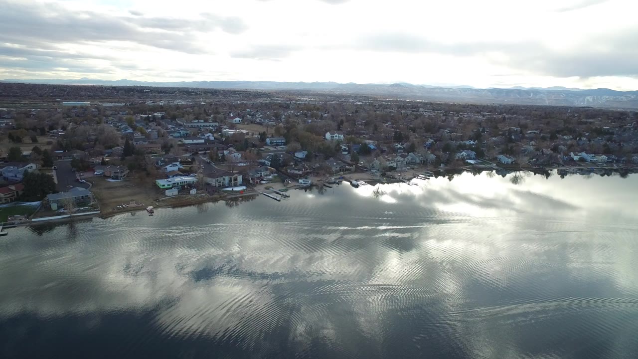 Aerial view over reflective water toward shoreline homes and a suburban grid.
