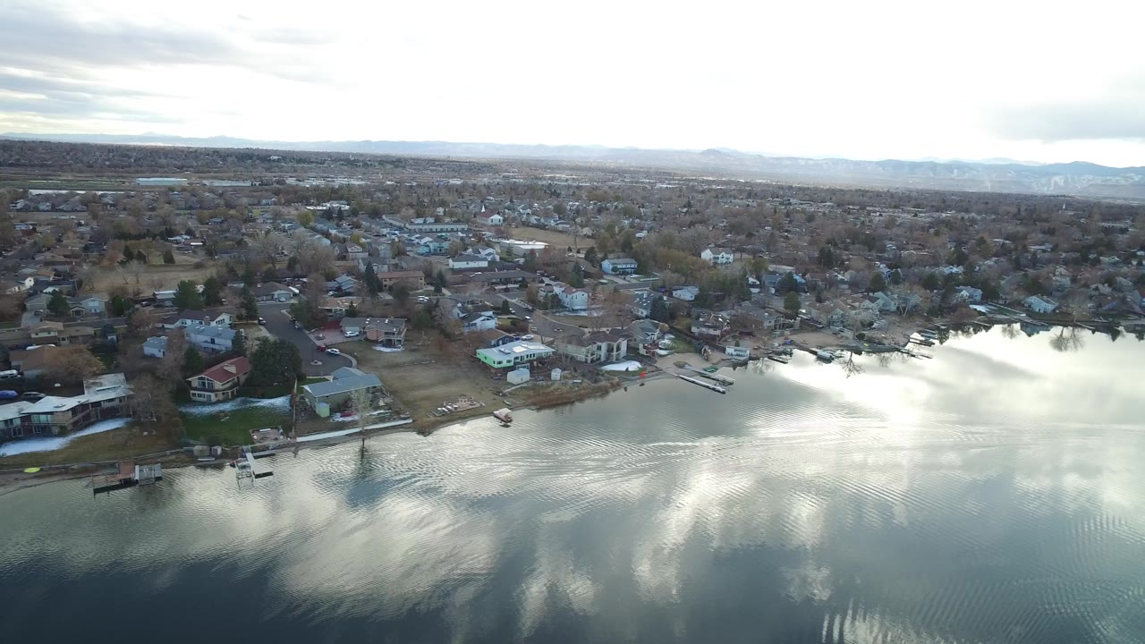 Westminster, Colorado aerial frame with bright cloud reflection on the water, small docks along the shore, residential roofs, bare trees, and no visible people.