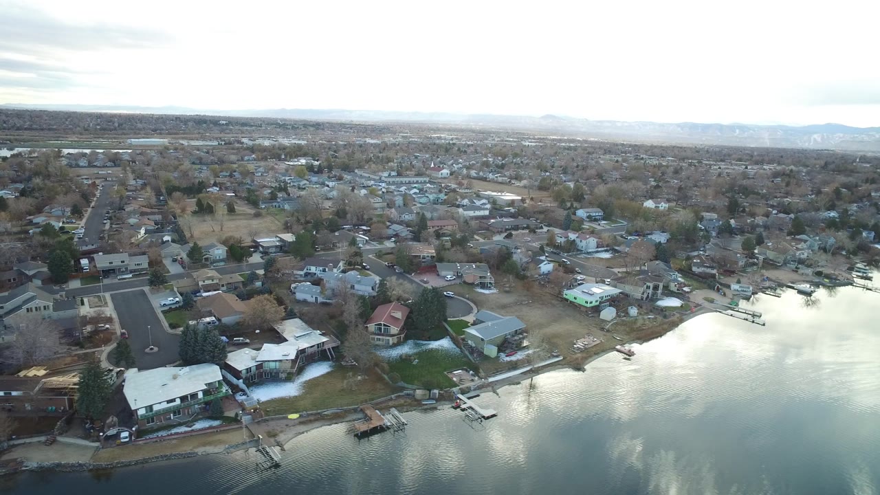 Elevated suburban lakefront view with houses, docks, roads, and winter trees.