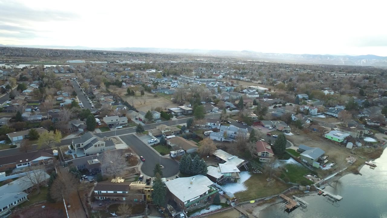 High aerial view of Westminster, Colorado homes, intersecting residential streets, bare trees, and distant low hills, with no visible people.