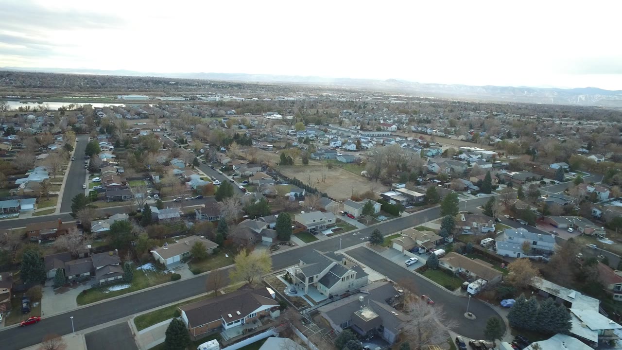 Opening aerial frame over Westminster, Colorado residential blocks, with intersecting roads, detached homes, bare trees, distant water, and no visible people.