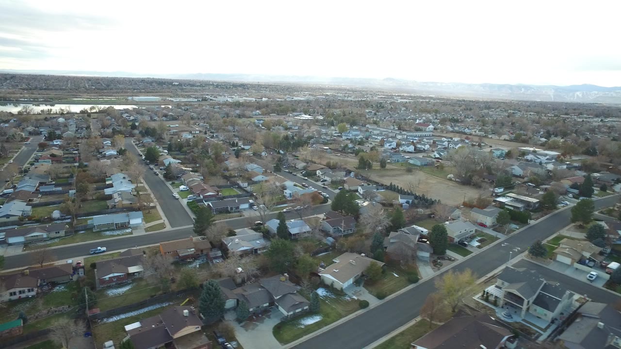 Aerial view across Westminster, Colorado residential blocks, with open ground beyond the houses, a bright horizon, and no visible people.