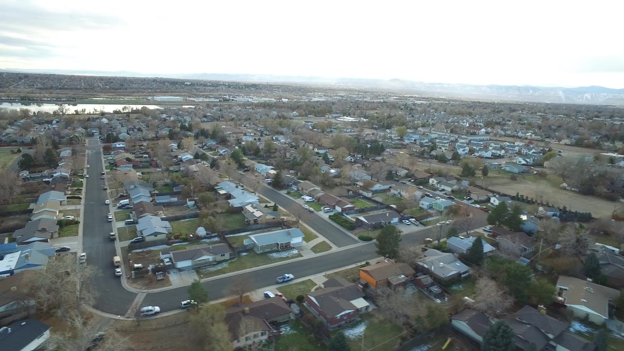Aerial view over residential streets, homes, trees, and distant water.